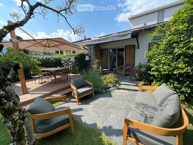 Outdoor seating with chairs and table, umbrella, stone patio, wooden deck, shrubs, small garden