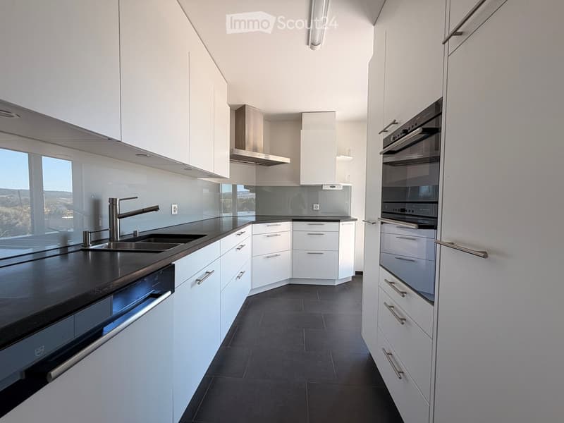 Modern kitchen with white cabinets, black countertops, stainless steel sink, and built-in oven. Features large windows with a scenic view.