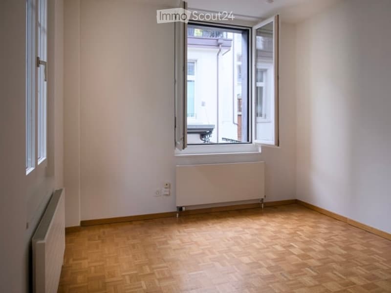 Empty room with wooden floors, white walls, and two large windows. There are two white radiators on the wall.
