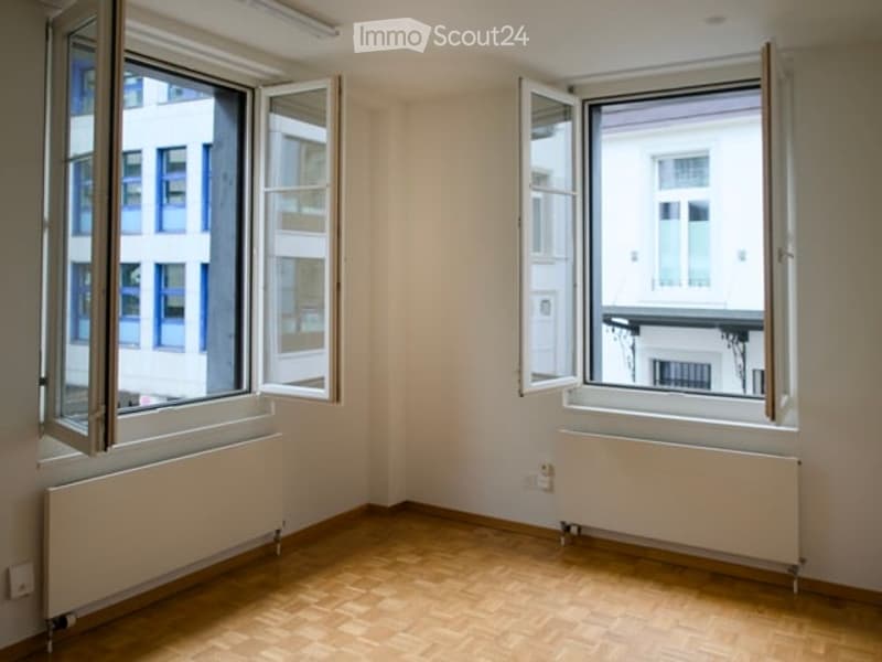 Empty room with wooden floors, white walls, and two large windows. There are two white radiators on either side of the room.