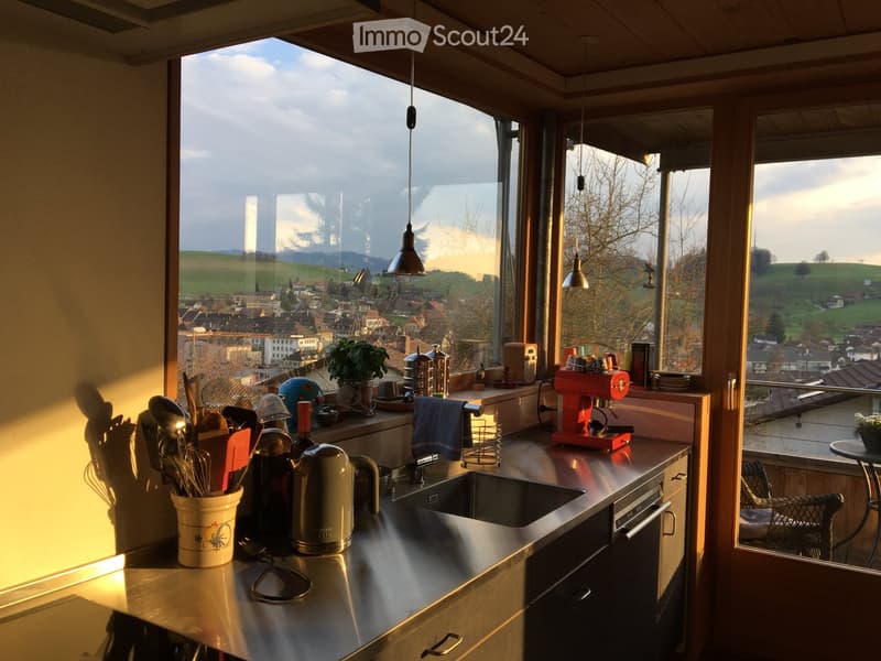 Modern kitchen with stainless steel countertops, large windows, and a view of the city and hills.