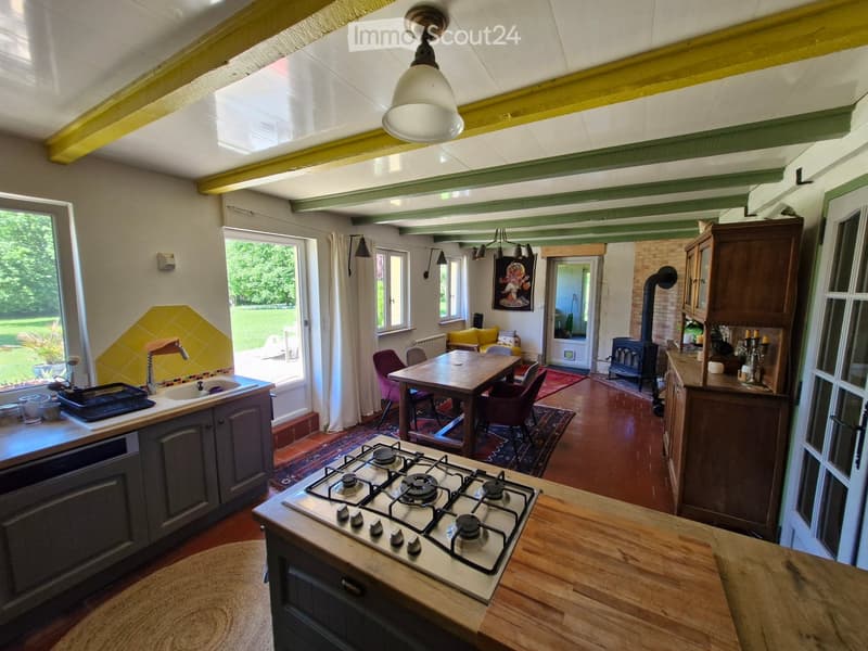 Furnished Room. Open-plan kitchen and dining area with wooden floors, gas stove, sink, wooden dining table, chairs, and wooden cabinets.