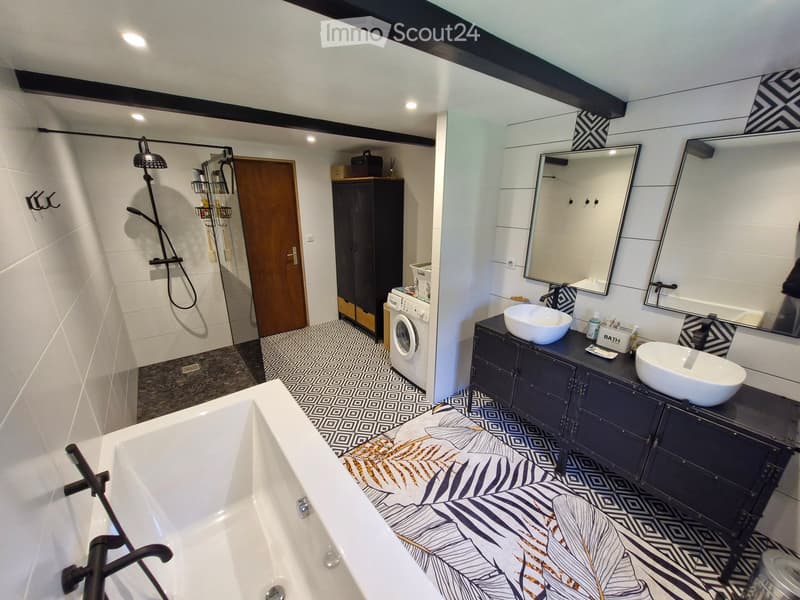 Bathroom. Modern bathroom with a large bathtub, double sink vanity, shower area, and a washing machine in the corner. Features geometric patterned tiles and sleek fixtures.