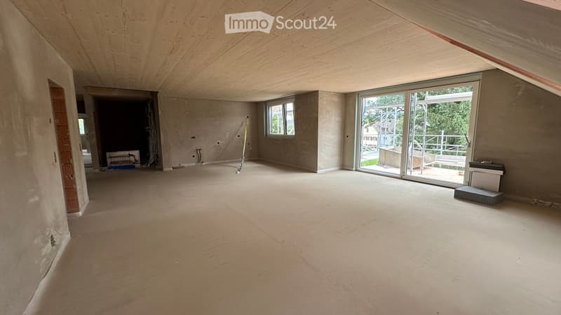 Empty room with unfinished walls and ceiling, large window, sliding glass door leading to balcony, and some construction materials visible.