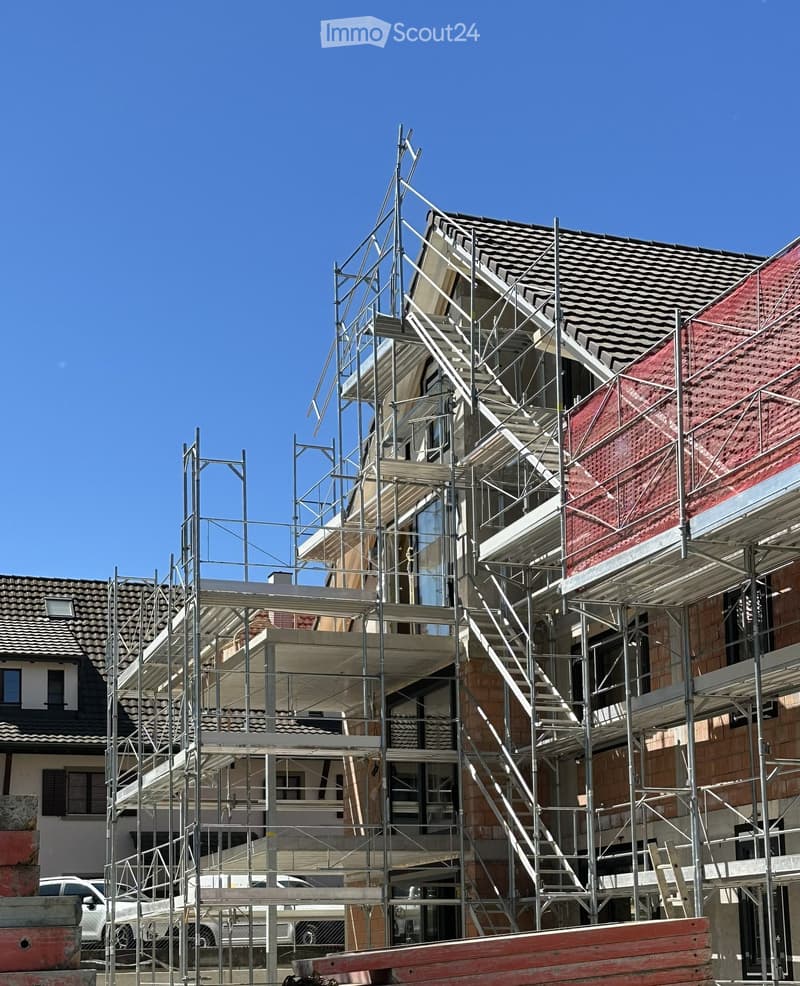 Building. A modern house under construction with scaffolding, exposed steel framework, and partially completed roofing.