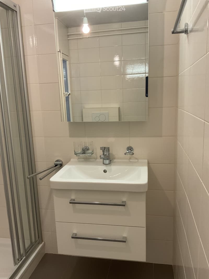 Bathroom. Modern bathroom with a white sink, chrome faucet, mirror, and two cups on the counter. Light beige tiles and a dark floor.