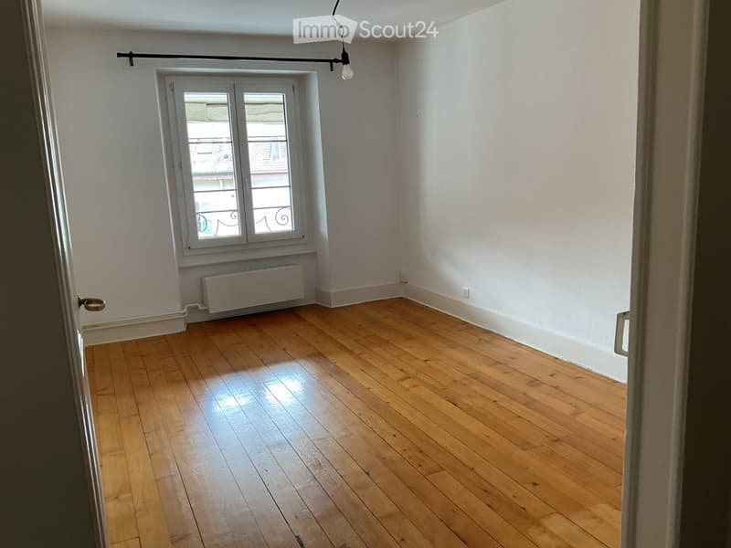 Unfurnished Room. Empty room with wooden flooring, white walls, a window with a view of a balcony, and a radiator below the window.