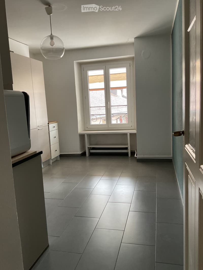 Unfurnished Room. Empty hallway with tiled floor, white walls, a small table near a window, and a hanging light fixture.