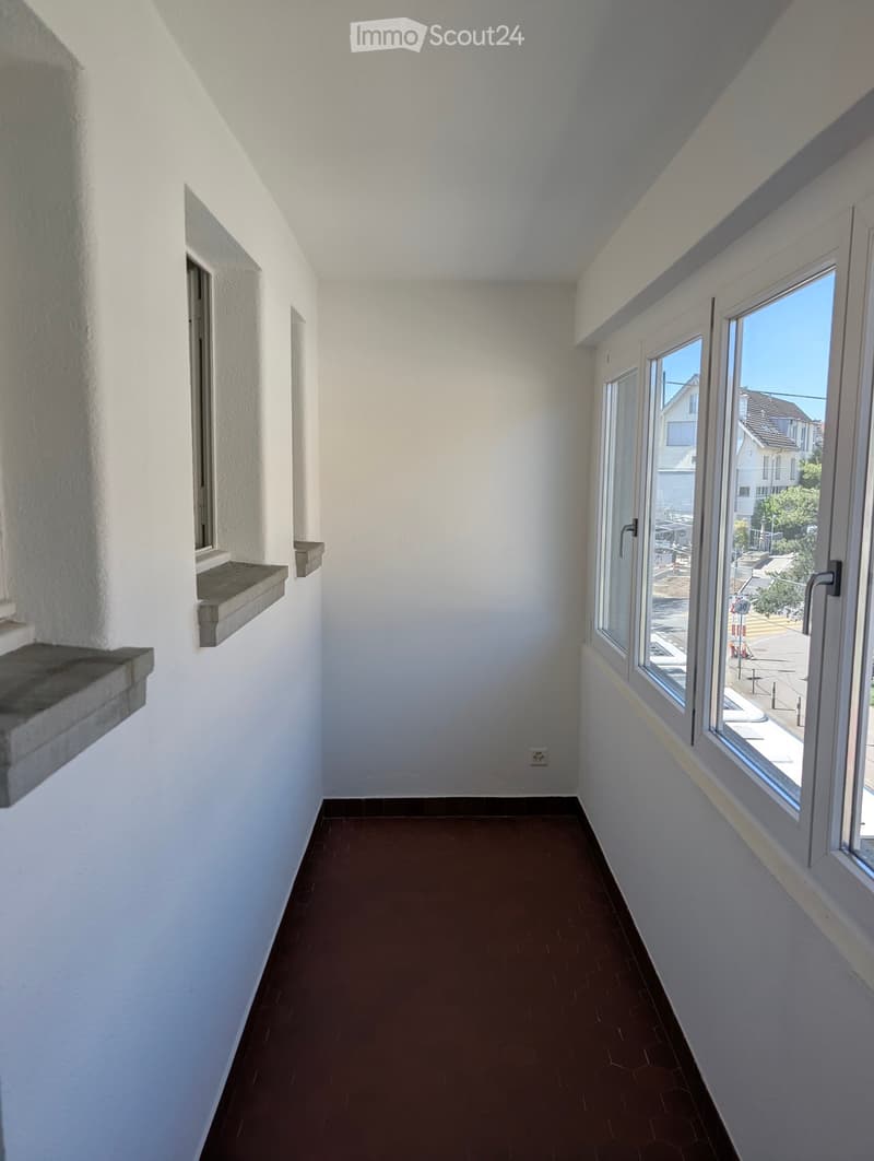 Empty room with white walls, brown floor, three windows, power outlet