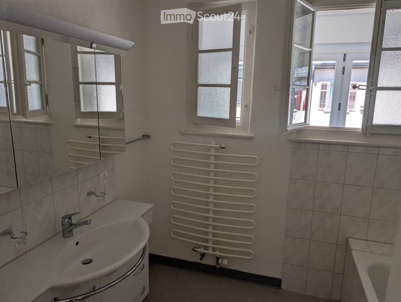 Bathroom with white tiles, white sink, mirror, bathtub, and a window.