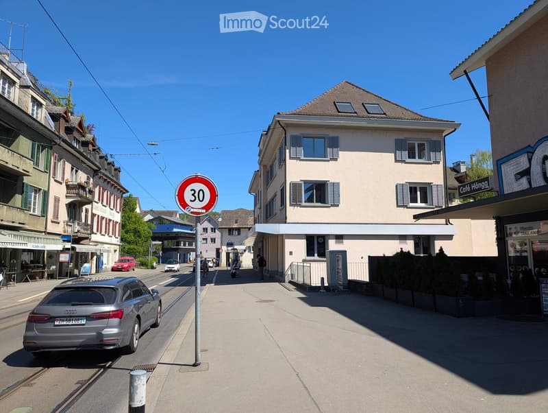Urban street with a speed limit sign, buildings, parked cars, and pedestrians.