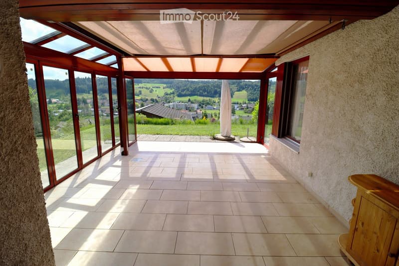 Bright sunroom with large glass windows and doors, tiled floor, and a scenic countryside view.