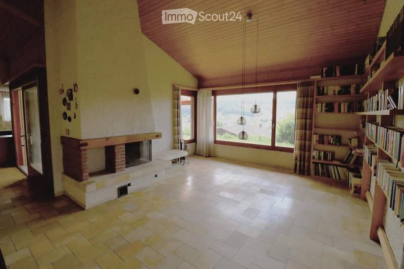 Bright living room with a brick fireplace, large windows offering a scenic view, and built-in wooden bookshelves filled with books.