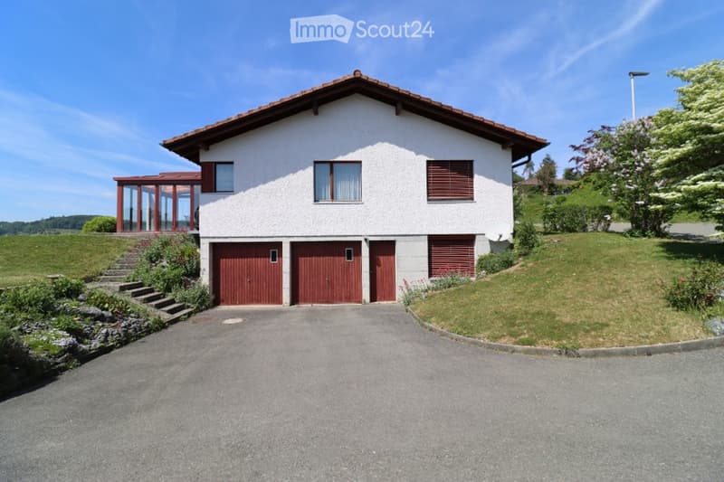 Two-story white house with red garage doors, a covered porch, and a well-maintained lawn.