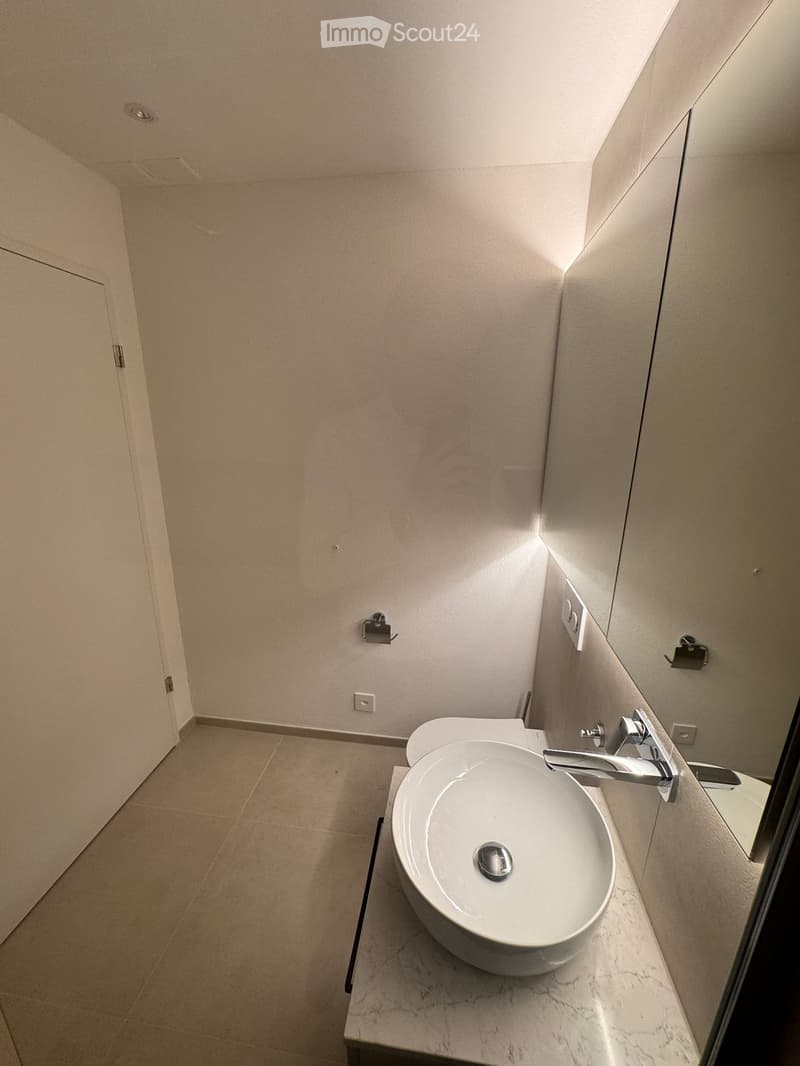 Modern bathroom with a white sink, chrome faucet, and toilet. Light-colored tiles and marble countertop.