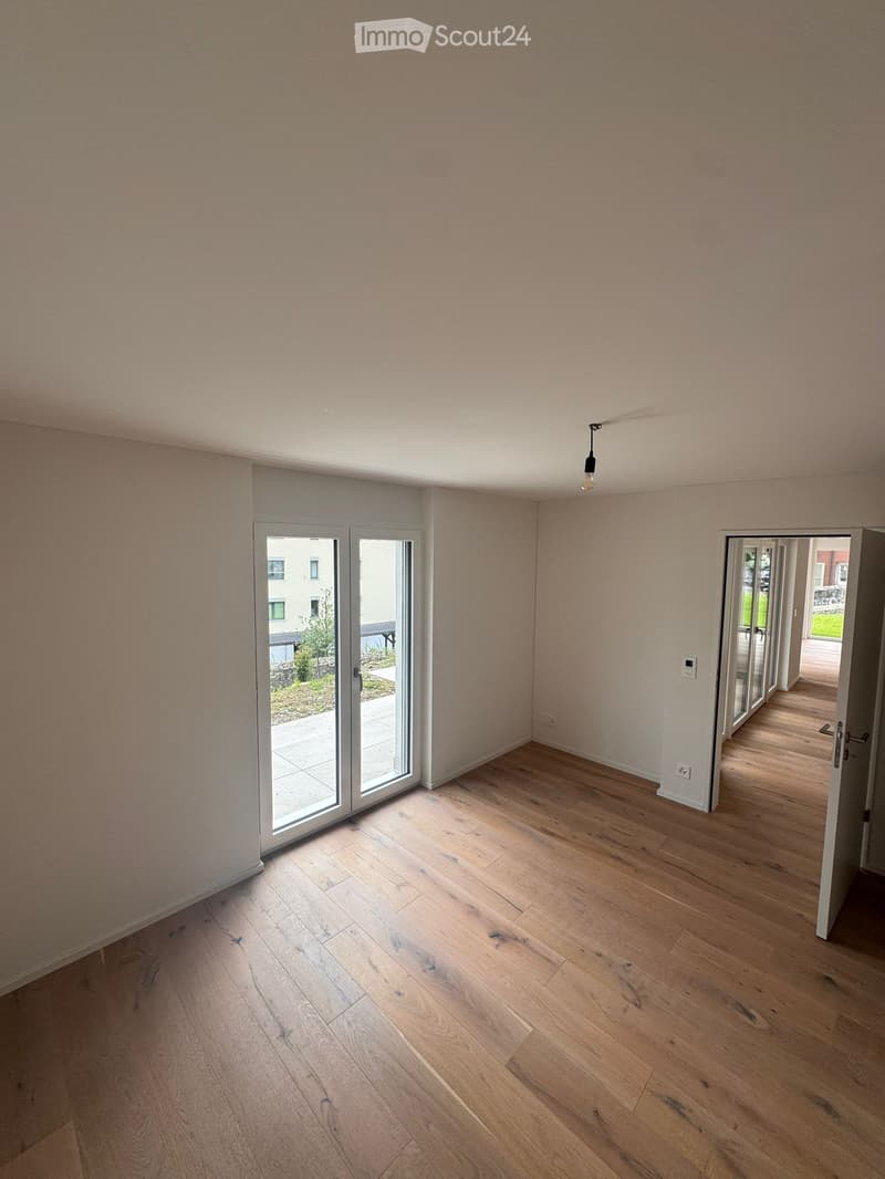 Empty room with light wooden flooring and white walls, featuring large sliding glass doors leading to an outdoor area.