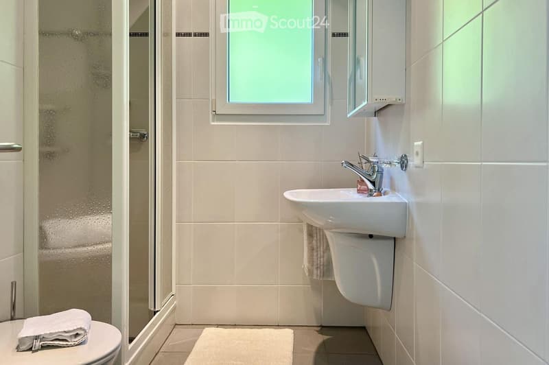 white tiled walls, white floor, white toilet, white shower, white sink, white towel rack, clear shower door