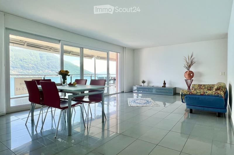 large windows, dining table, 6 chairs, blue sofa, small plant, balcony, vase, tiles floor