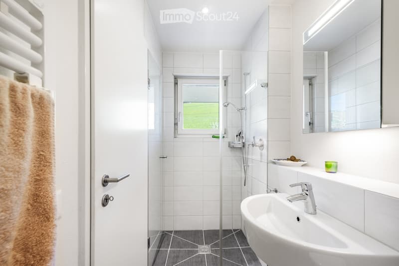 Bathroom. Modern bathroom with white tiles, a glass-enclosed shower, a sink with a modern faucet, a large mirror, a towel on a rack, and a candle on the windowsill.