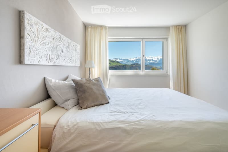 Bedroom. Modern bedroom with a large bed, pillows, nightstand, lamp, and scenic mountain view through large windows.