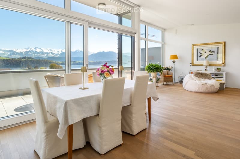 Furnished Room. Bright dining area with large windows offering a scenic mountain view, featuring a dining table with chairs, table lamps, potted plants, a sofa, and a picture frame on the wall.