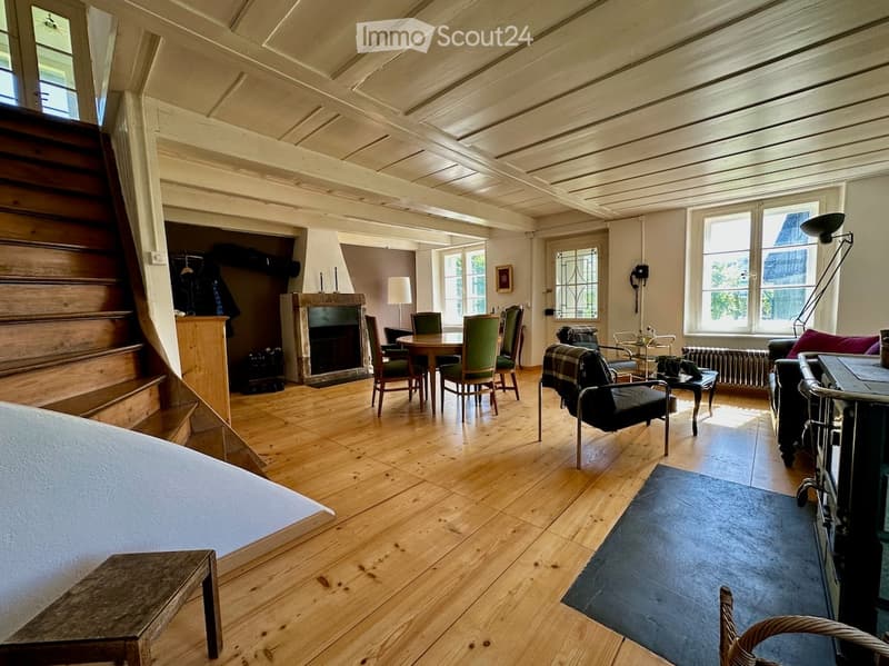 Furnished Room. Spacious living room with wooden floors, fireplace, large windows, and various seating arrangements including a sofa, chairs, and a small table.