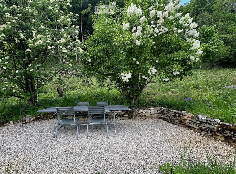 Garden / Outdoor Area. Garden area with a stone wall, gravel ground, and a table with chairs surrounded by lush greenery and flowering trees.