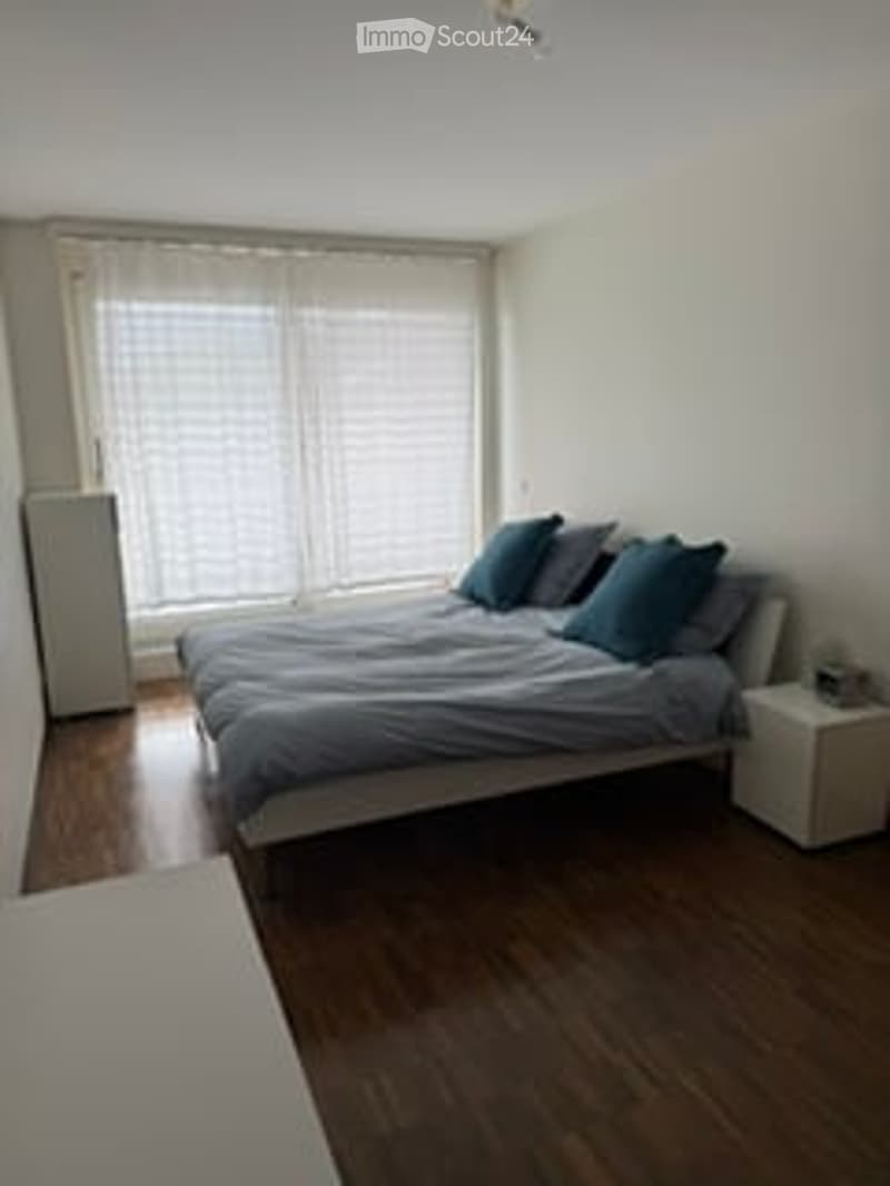 Bedroom. Bright bedroom with wooden flooring, a double bed with blue pillows and a nightstand, large windows with blinds.