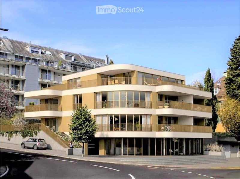 Building. Modern multi-story residential building with large windows, balconies, and a curved facade. The building features a combination of beige and yellow tones, with a staircase leading up to the entrance.