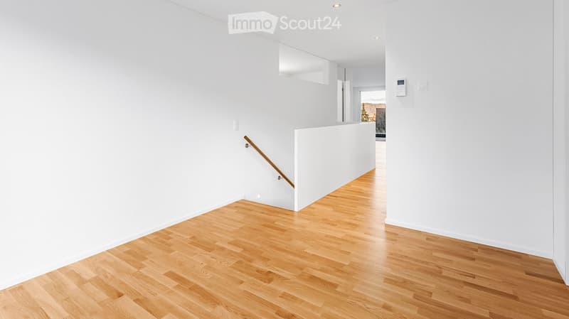 Corridor / Hallway. Bright, minimalist hallway with light wooden flooring and white walls. Features a staircase with a wooden handrail and a small built-in shelf on the wall.