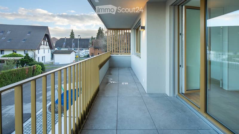Balcony / Terrace. Balcony with modern glass sliding doors, beige tiled floor, and a golden metal railing overlooking a residential neighborhood.