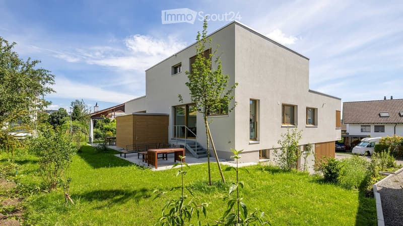 House. Modern two-story house with white exterior, large windows, and a small garden area with a wooden table and chairs.