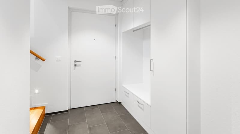 Corridor / Hallway. A modern, minimalist hallway with white walls, grey tiled flooring, a white door, built-in white storage units with drawers, and a wooden handrail on the left side.