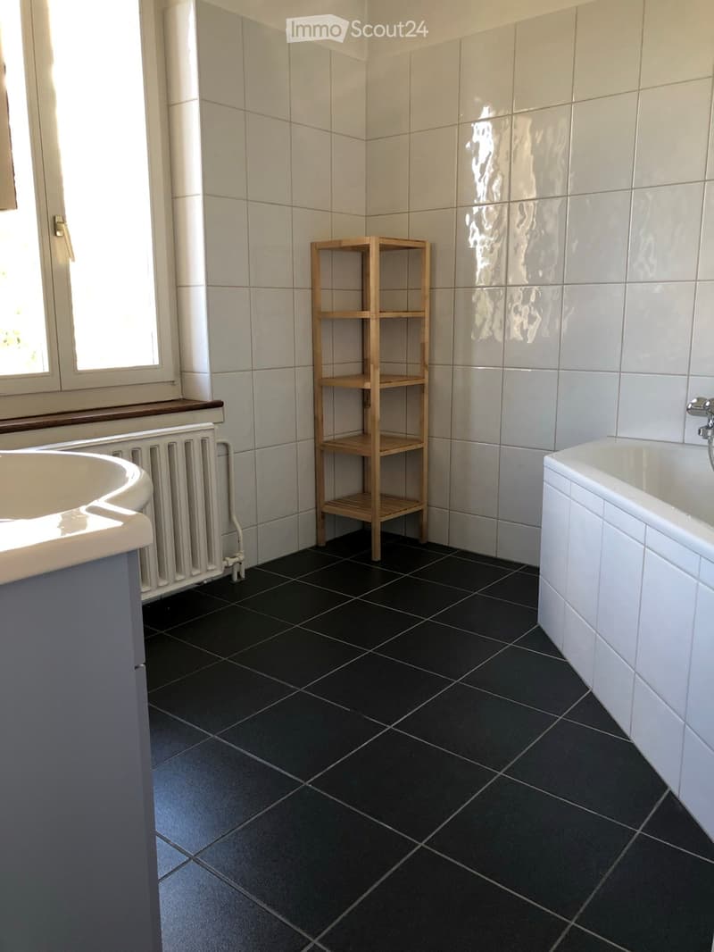 Bathroom with white tiles, black floor tiles, a bathtub, a sink, and a wooden shelf.
