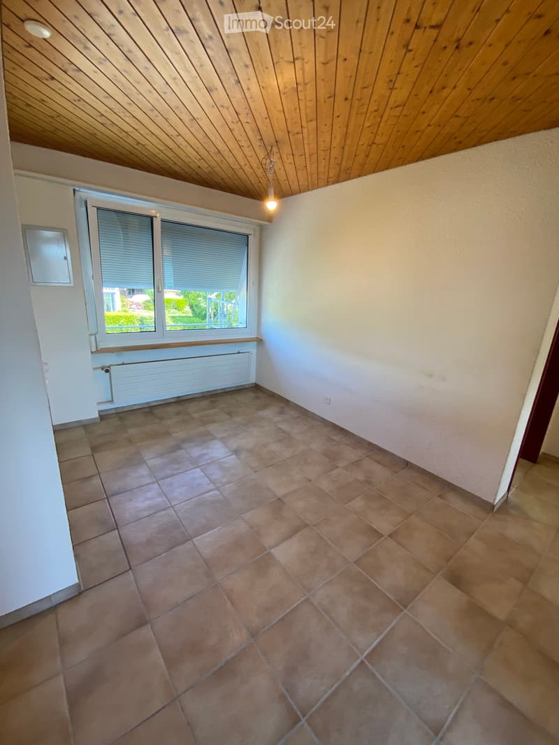 Empty room with tiled floor, wooden slanted ceiling, large window with blinds, radiator, and light fixture.