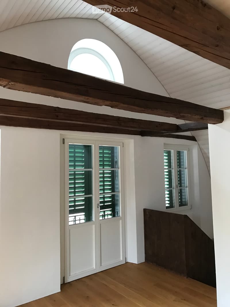 white walls, wooden beams, arched window, white door, wooden floor