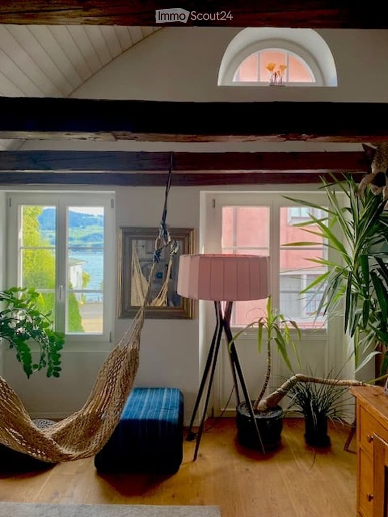 Interior of a cozy room with a hammock, a stand-alone lamp, framed picture, plants, and a small ottoman