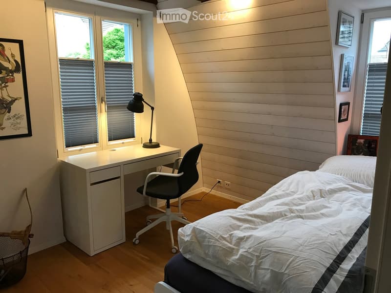 white desk, black lamp, black chair, bed, two pillows, wall mounted picture frames, trash can