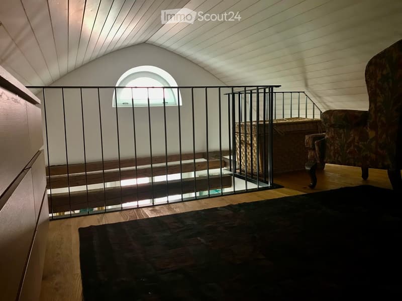 wooden floor, white walls, black railing, small window, wicker basket, chair, black carpet