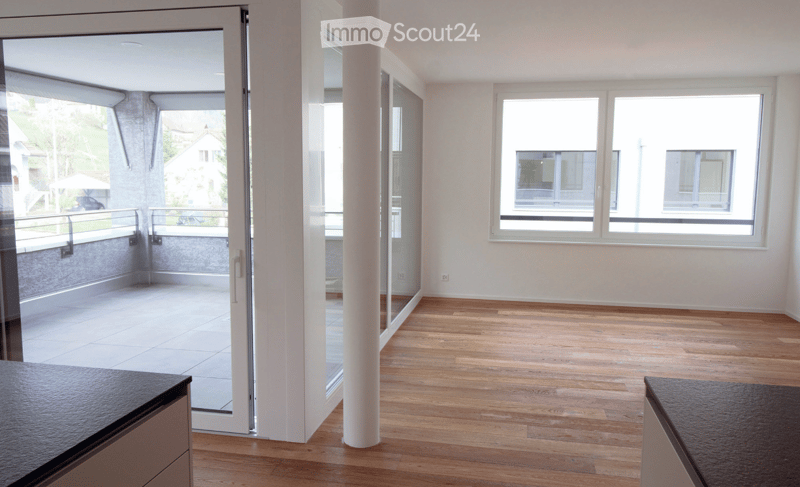 Empty room with wooden flooring, large windows, and a sliding glass door leading to a balcony.