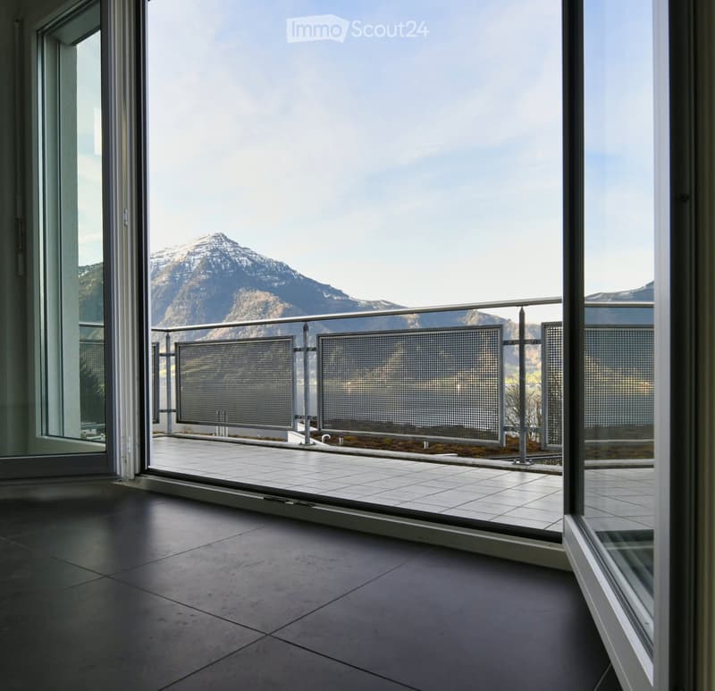 A balcony with tile floor and metal railings overlooking mountains and a lake
