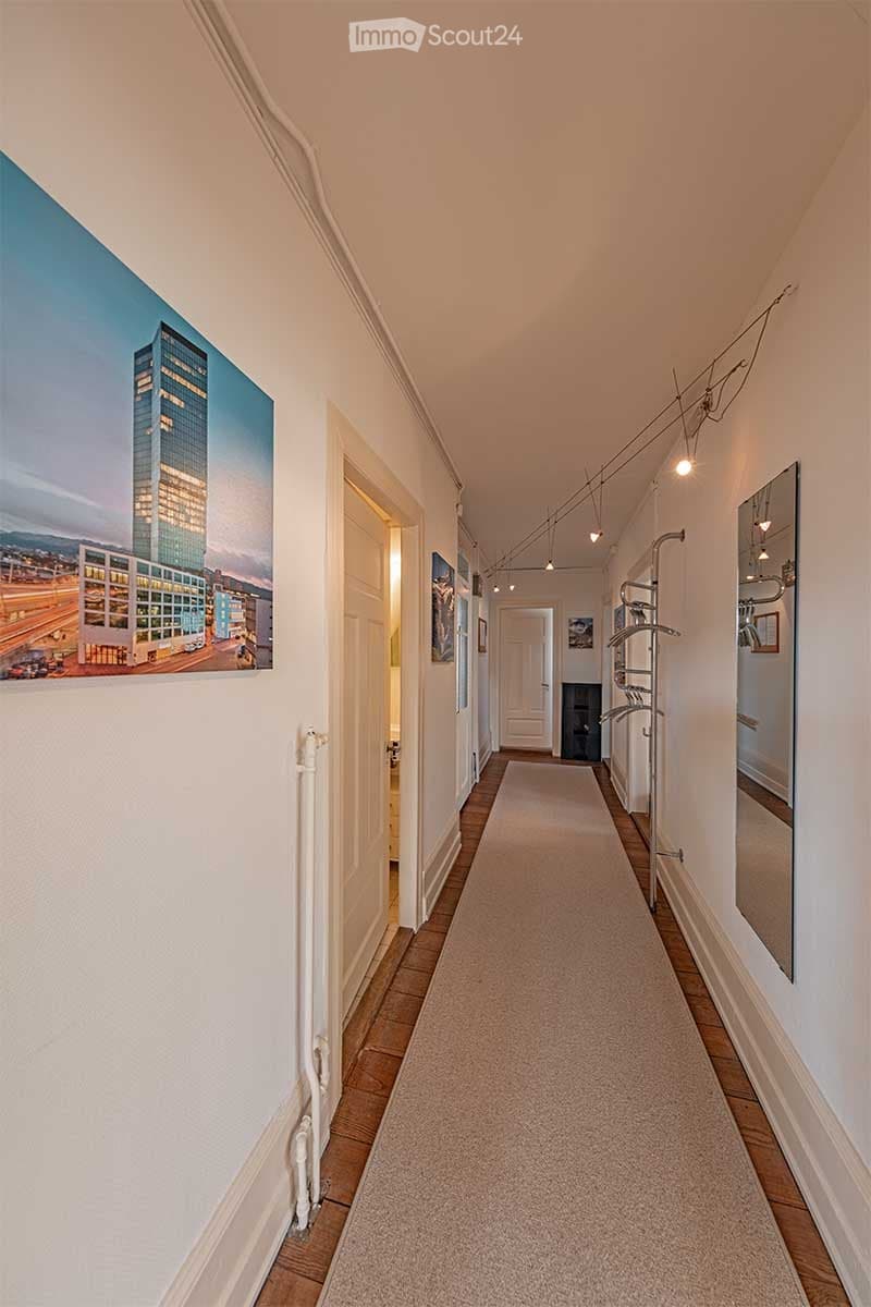 Long hallway, beige carpet, picture on the wall, radiator, and mirror