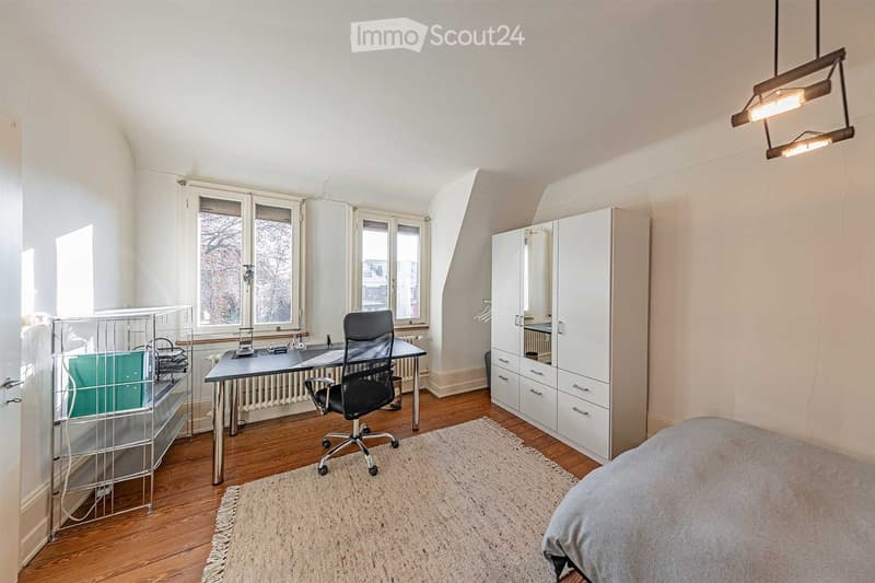An office room with a desk, office chair, small bed, metal file storage, white wardrobe, and carpet on the wooden floor