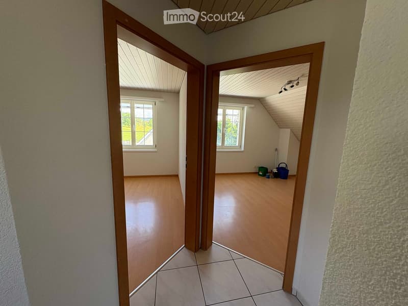 Empty hallway with wooden doors leading to two rooms, wooden flooring, and white walls.