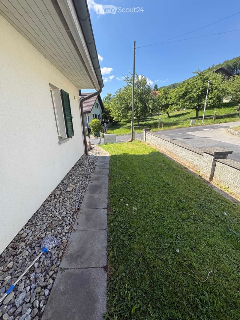 Sidewalk leading to a house with a gravel bed, grassy area, and a stone wall along the road.