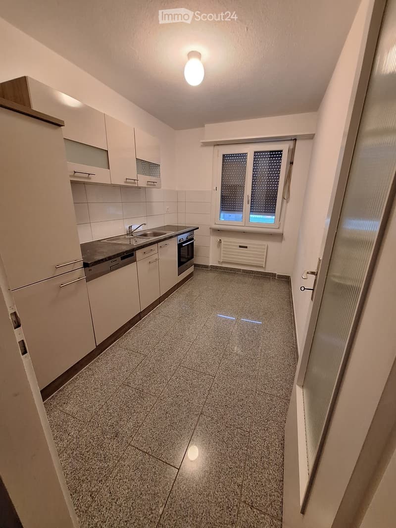 Modern kitchen with white cabinets, granite countertop, sink, oven, and dishwasher. Features a window with blinds and tiled flooring.