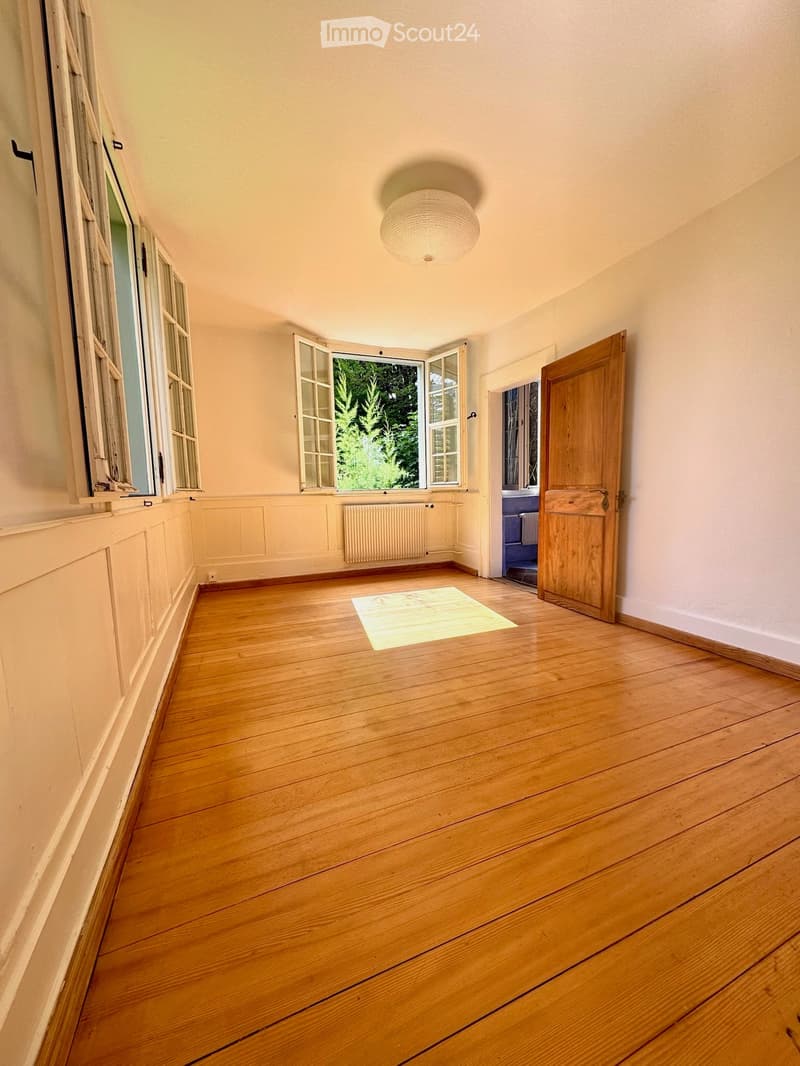 Empty room with wooden flooring, white walls, large windows, and a ceiling light fixture.