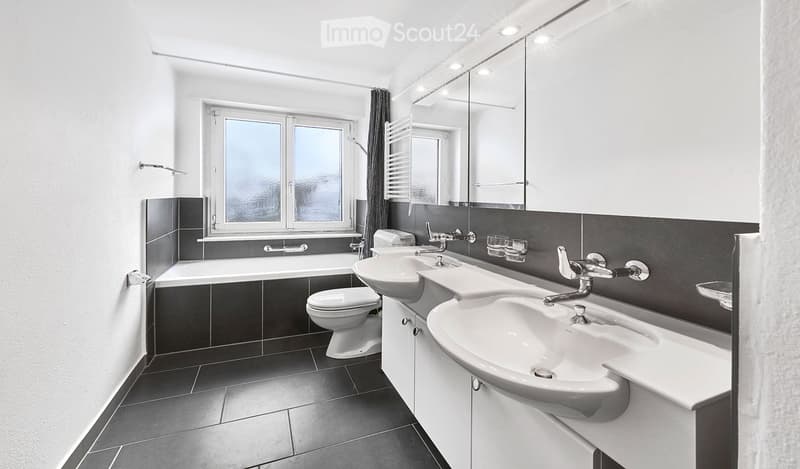 modern bathroom with white tiles, bathtub, two sinks, toilet, mirror, window