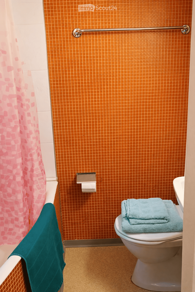 A bathroom with an orange tiled wall, a white bathtub, and a white toilet.