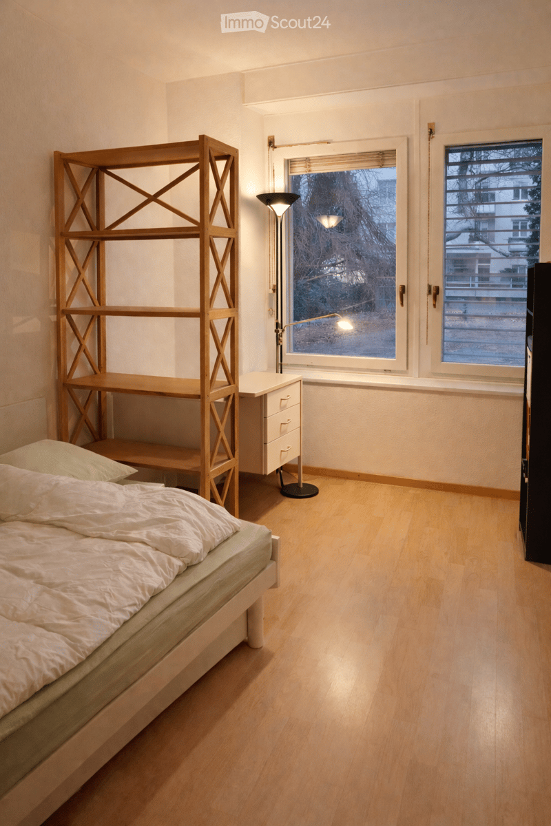 bedroom with double bed, wooden desk, lamp, shelves, windows with blinds